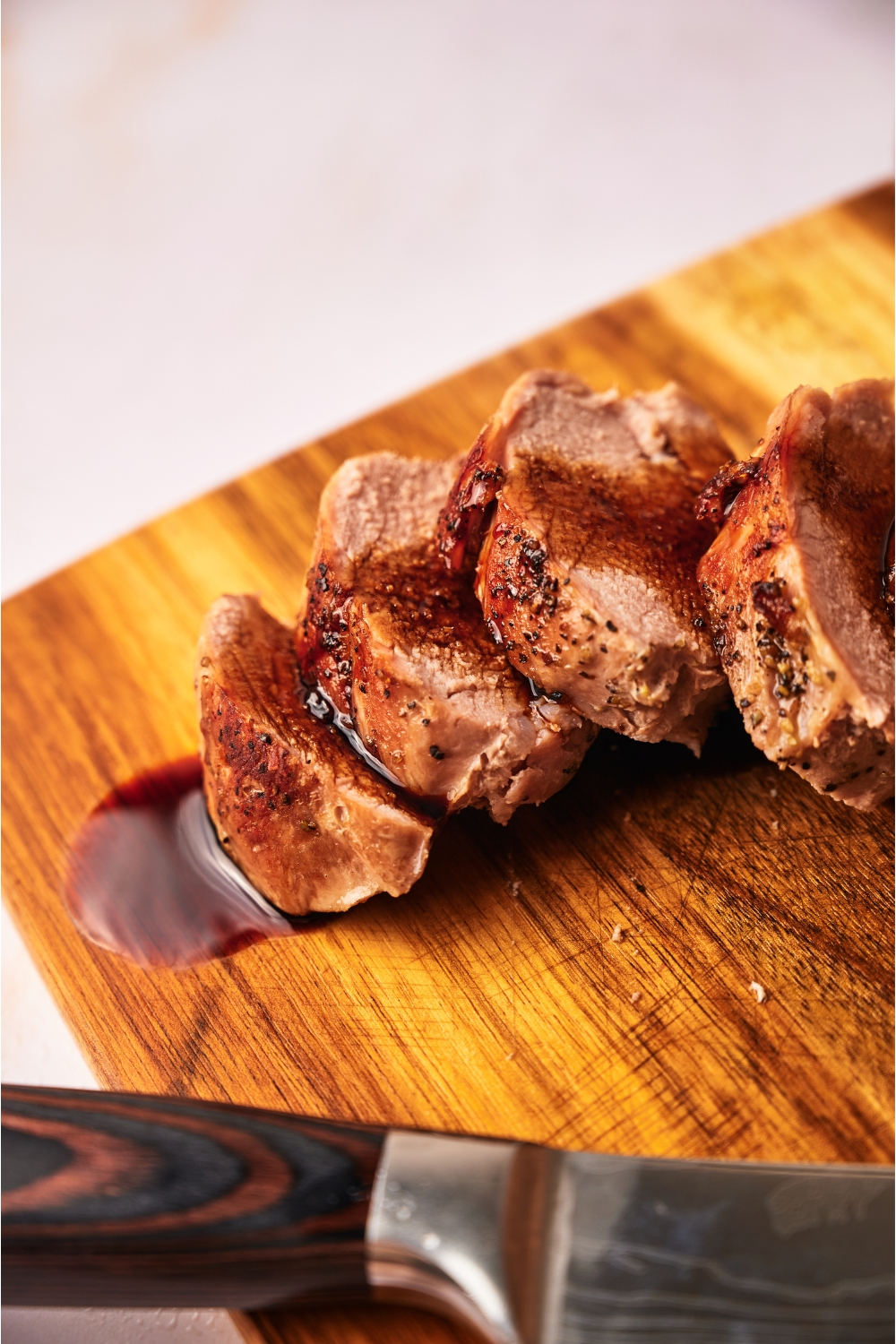 Close up of cooked pork tenderloin coated in a brown sauce atop a wood cutting board.
