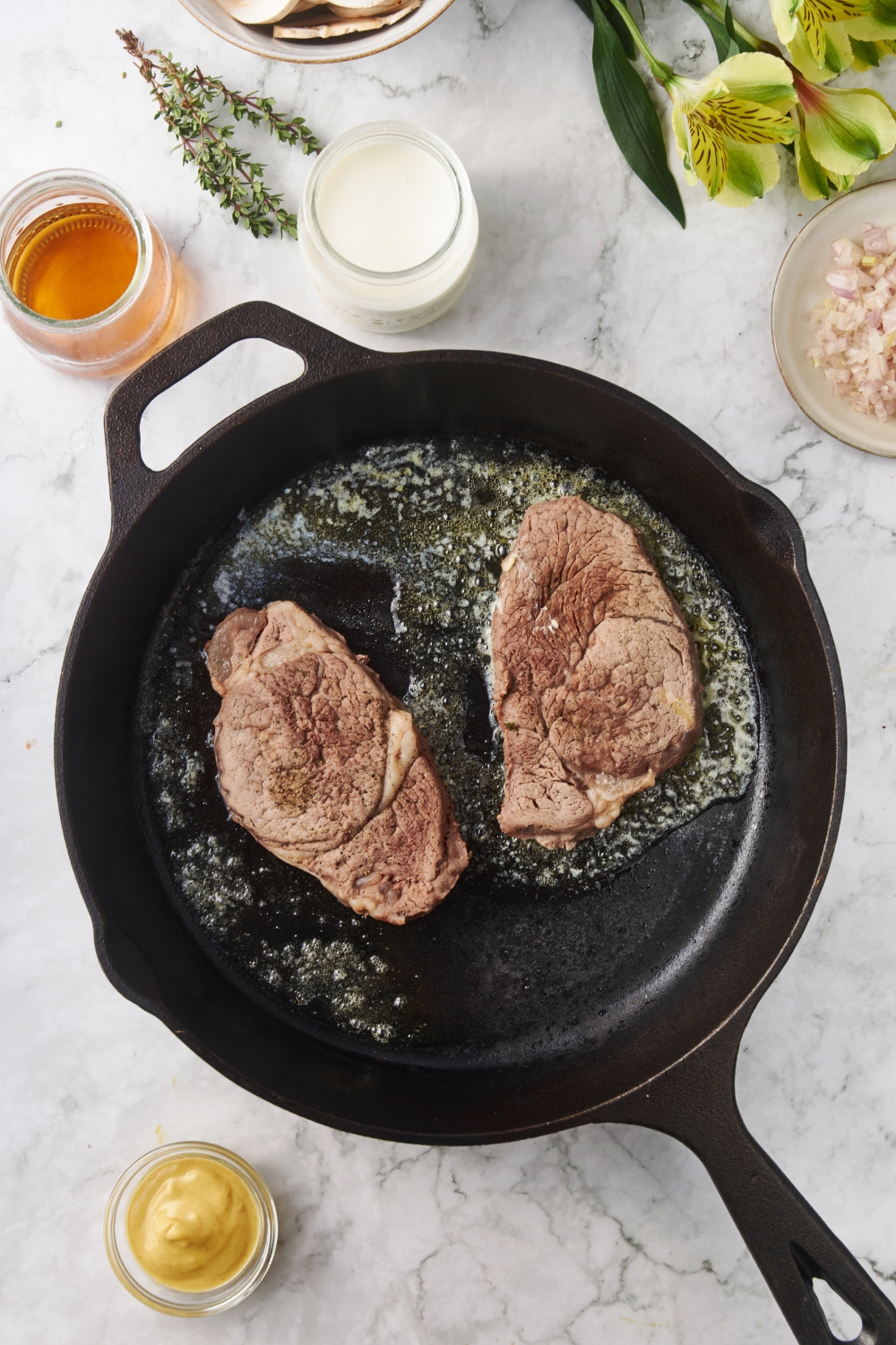 Two filet mignon steaks being seared in a cast iron skillet with melted butter.