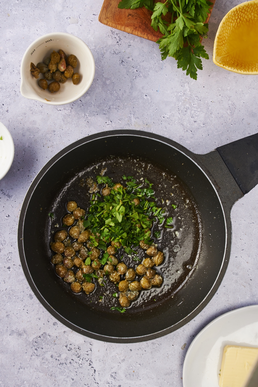 A black pot with capers and herbs cooking in oil.