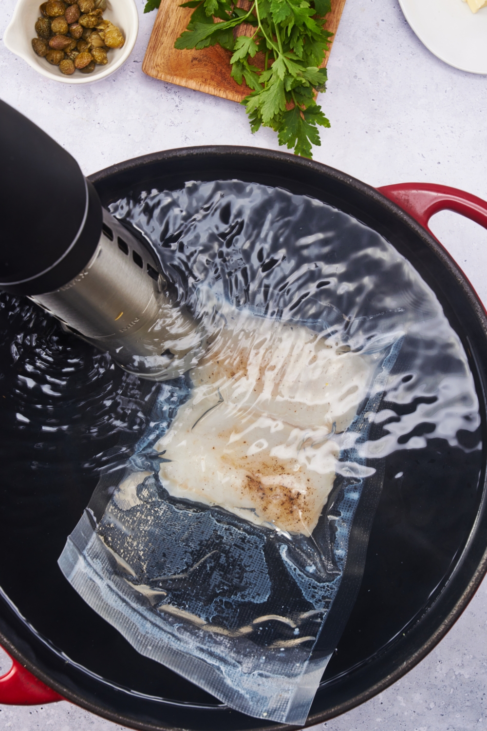 A halibut fillet in a vacuum-sealed bag in a water bath with a sous vide machine in the pot of water.