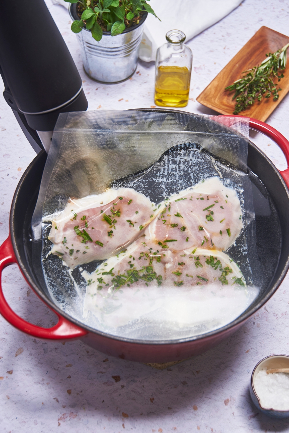 Pork chops being sous vide with fresh herbs in a large pot of water.
