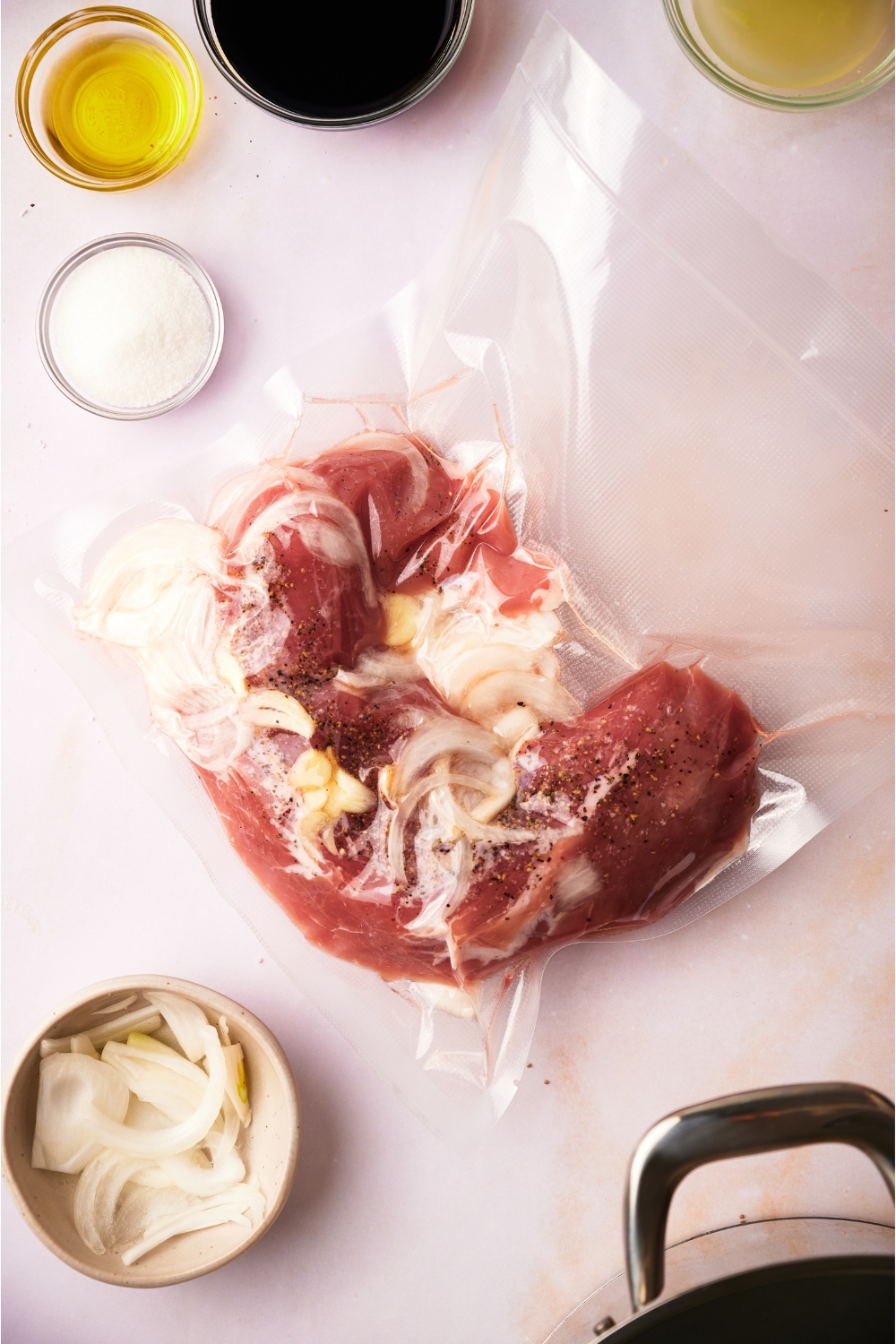 Pork tenderloin vacuum sealed with garlic and onion, surrounded by an assortment of ingredients.