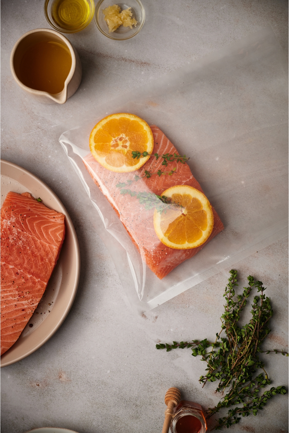 A salmon loin in a plastic bag with two orange slices and fresh herbs in the bag.