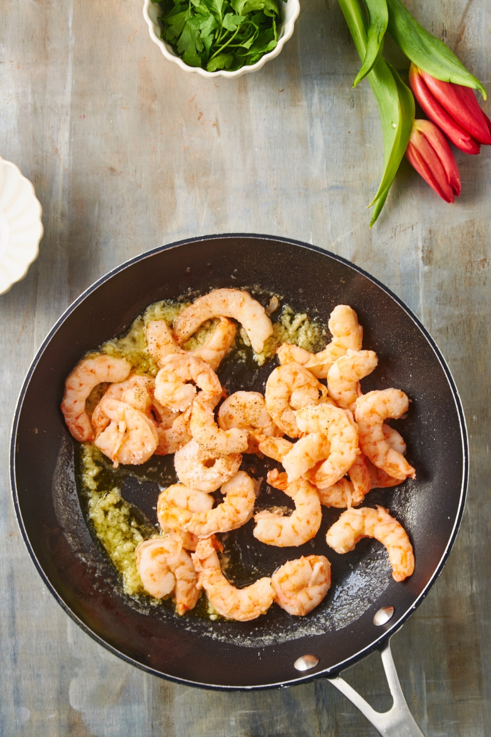 A black skillet filled with shrimp cooking in melted butter and minced garlic.