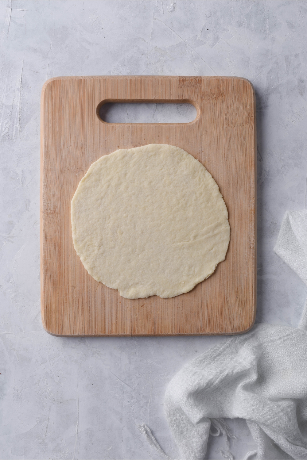 A flat disc of raw dough on a wood cutting board.