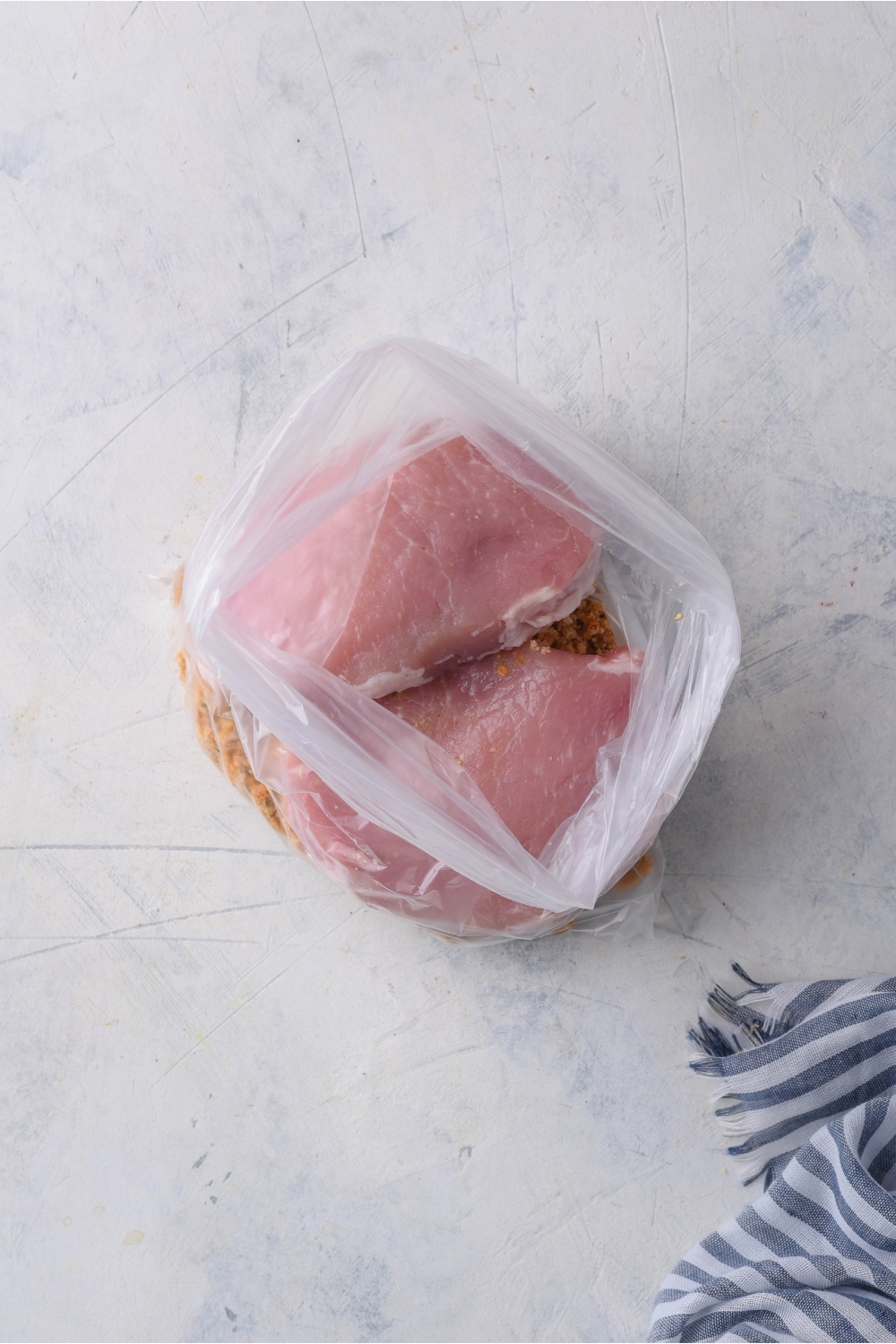 A clear plastic bag with two raw pork chops and a seasoning mixture in it.