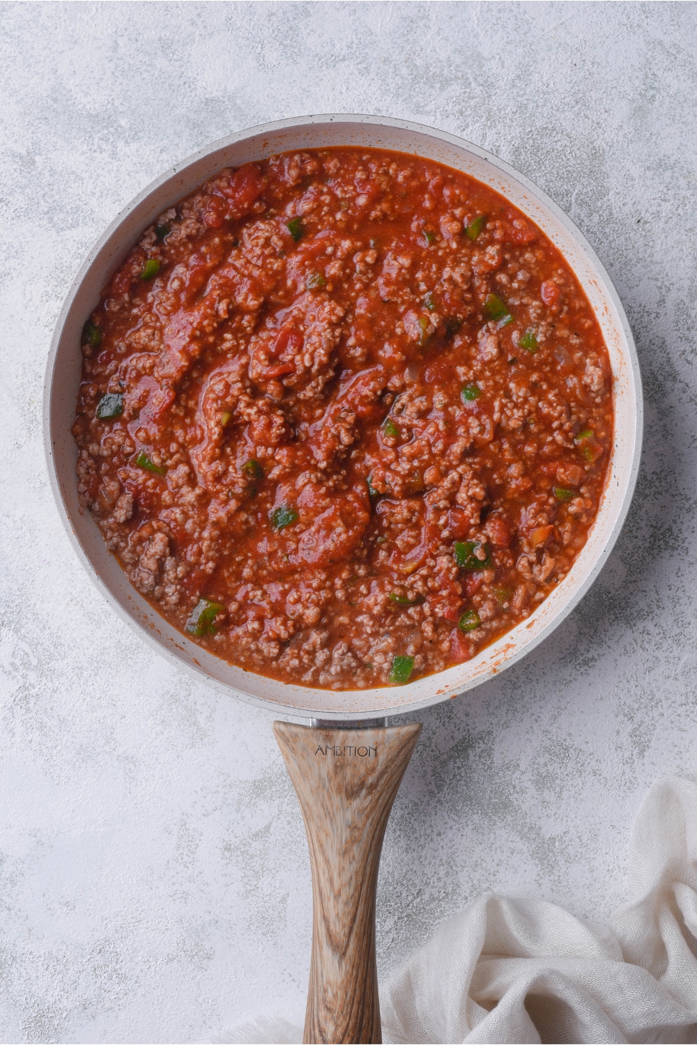 A grey skillet with a wood handle filled with coked brown beef and diced peppers in a thick tomato sauce.