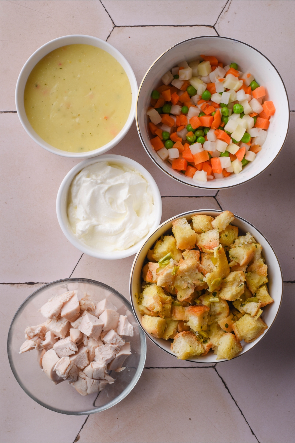 An assortment of ingredients including bowls of diced vegetables, cream of chicken soup, sour cream, cooked stuffing, and diced chicken.