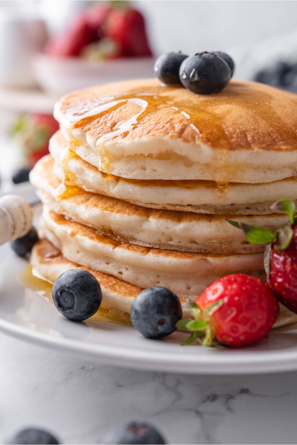 Close up of a stack of pancakes covered in maple syrup with berries on top of the pancakes and surrounding them on the plate.
