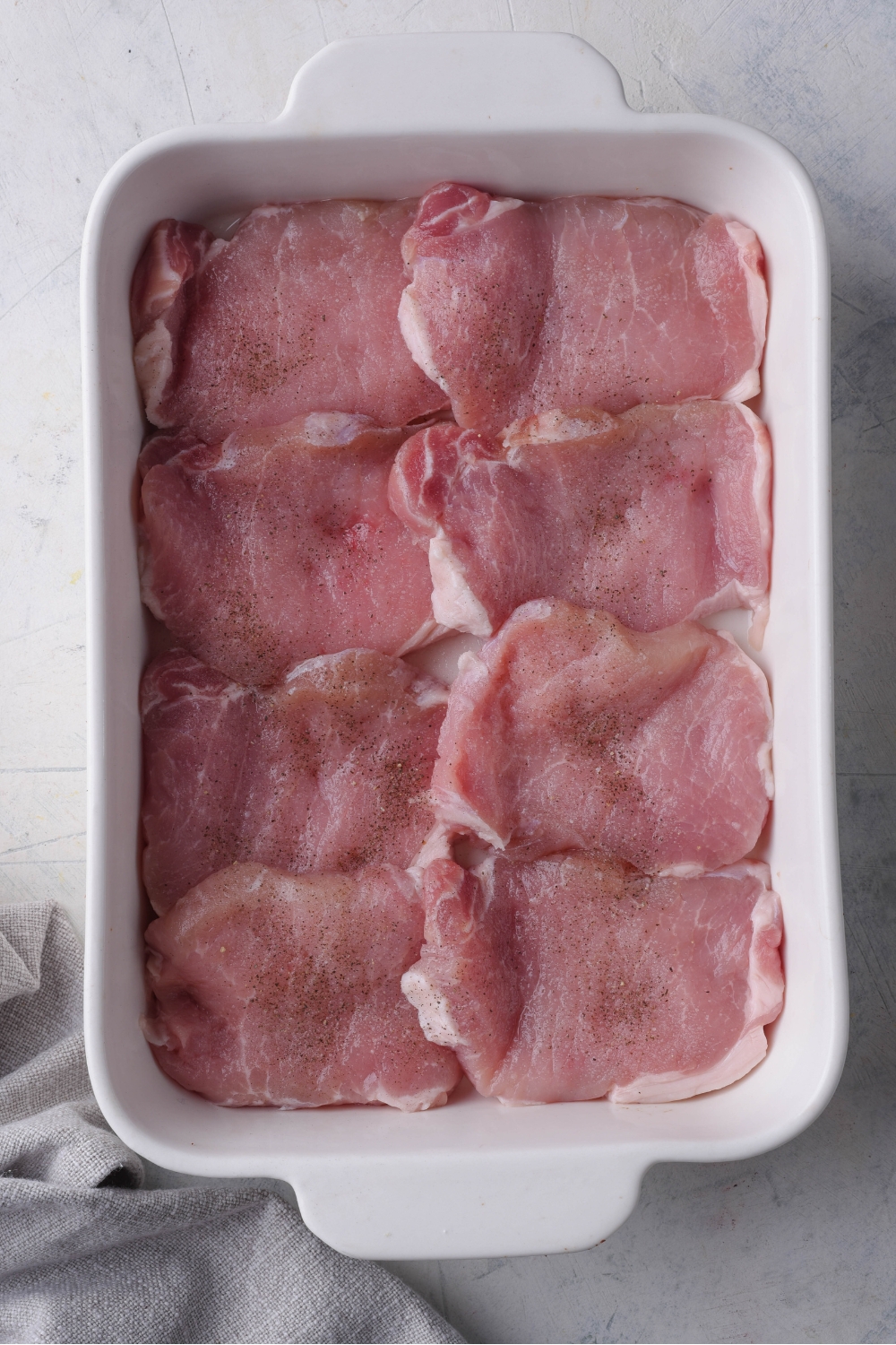 A white baking dish with raw pork chops layered on the bottom of the baking dish.