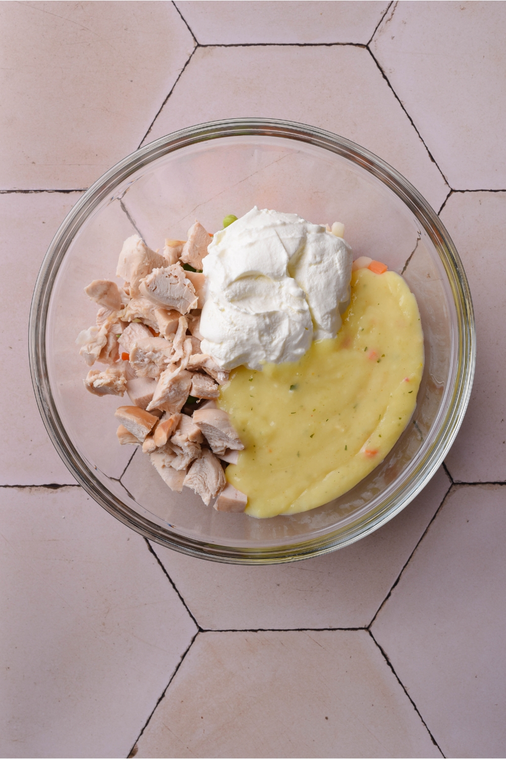 A white bowl with diced chicken, sour cream, and cream of chicken soup. The ingredients are separate and not yet mixed together.