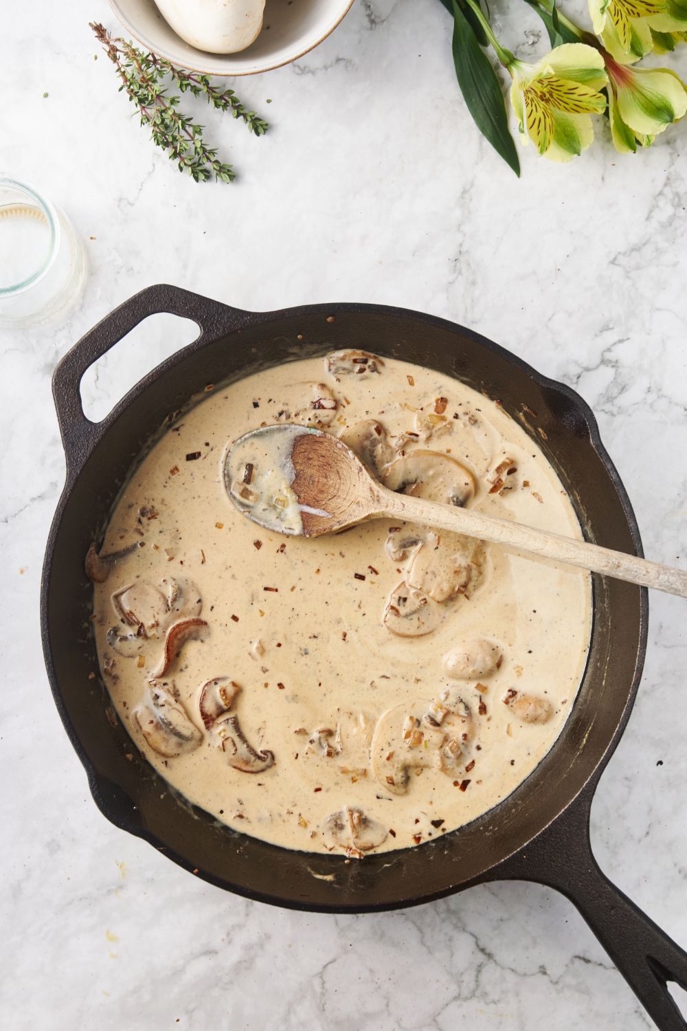 A cast iron skillet with a creamy brown sauce and mushrooms in it. There is a wooden spoon in the skillet covered in the sauce.
