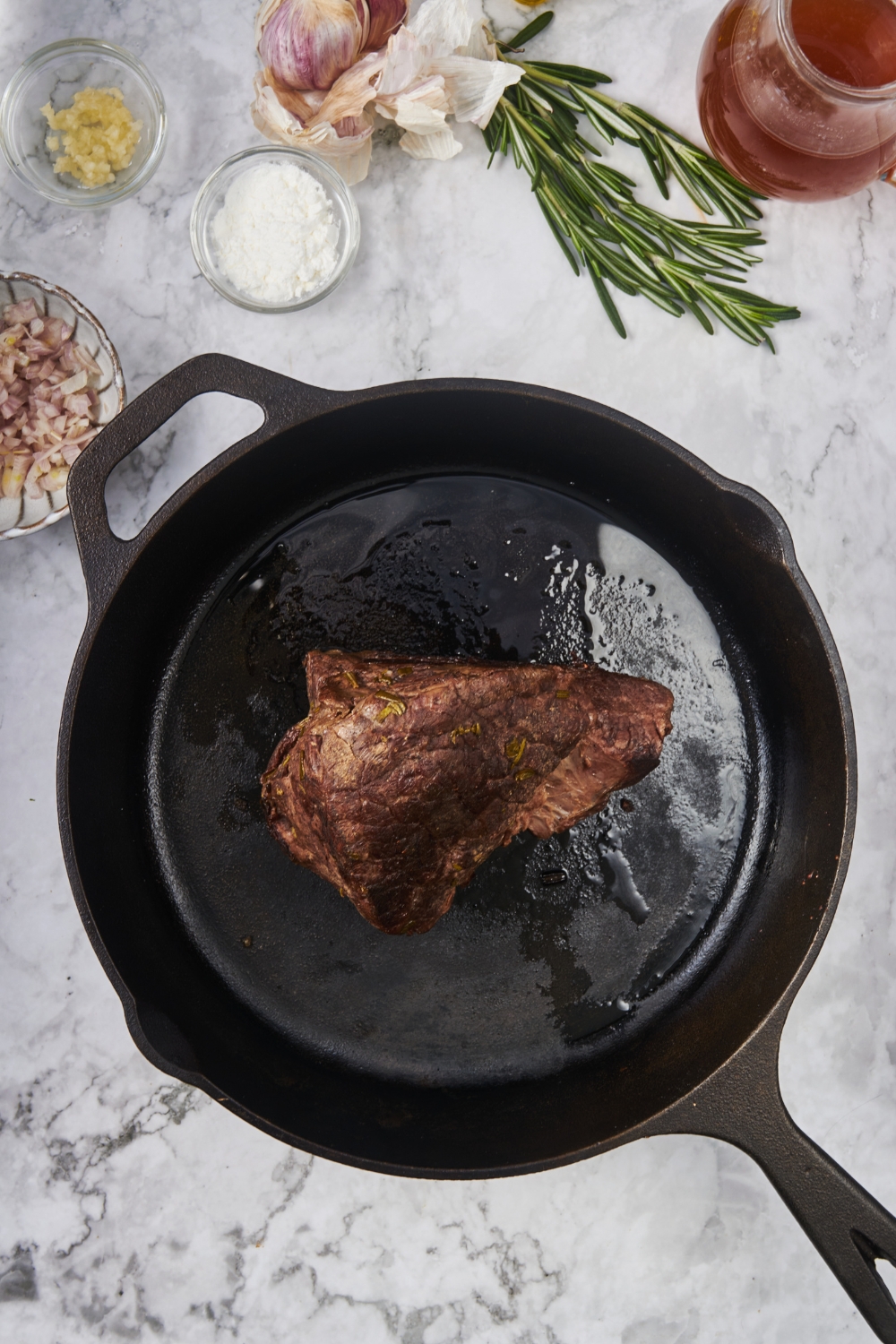 A black cast iron skillet with a seared chuck roast in it.