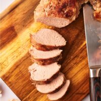 Sliced and cooked pork tenderloin on a wood cutting board.