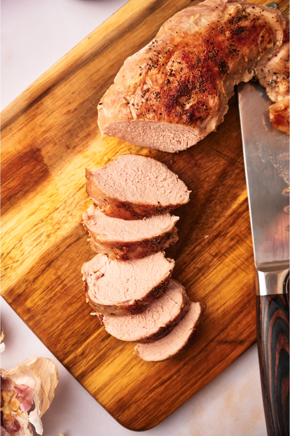 Sliced and cooked pork tenderloin on a wood cutting board.