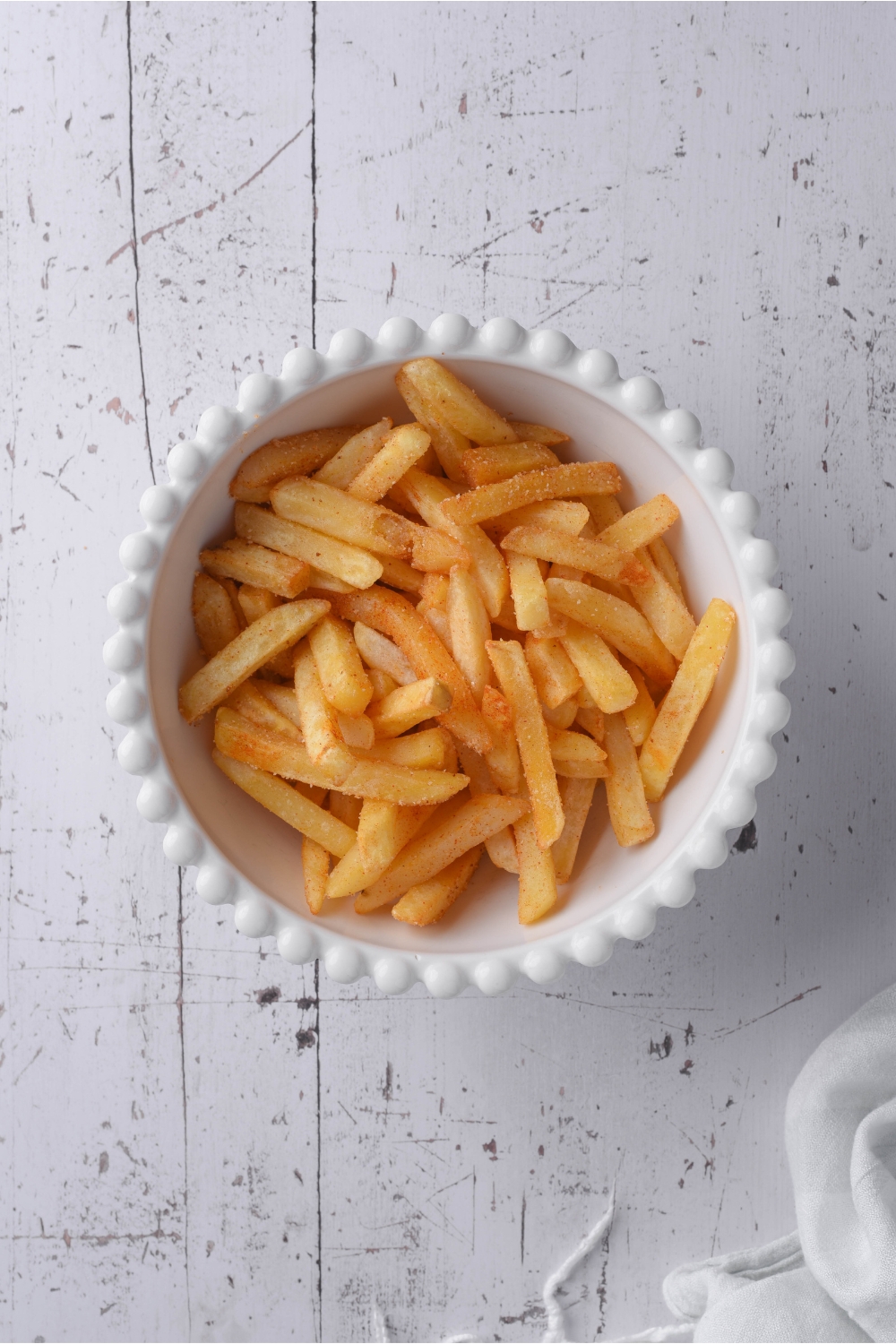A white decorative bowl filled with cooked seasoned french fries.