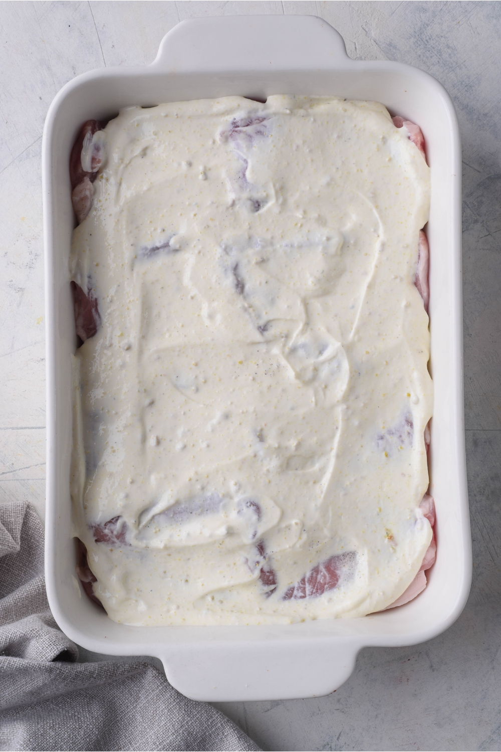 A white baking dish with raw pork chops and a sour cream mixture spread evenly across them.