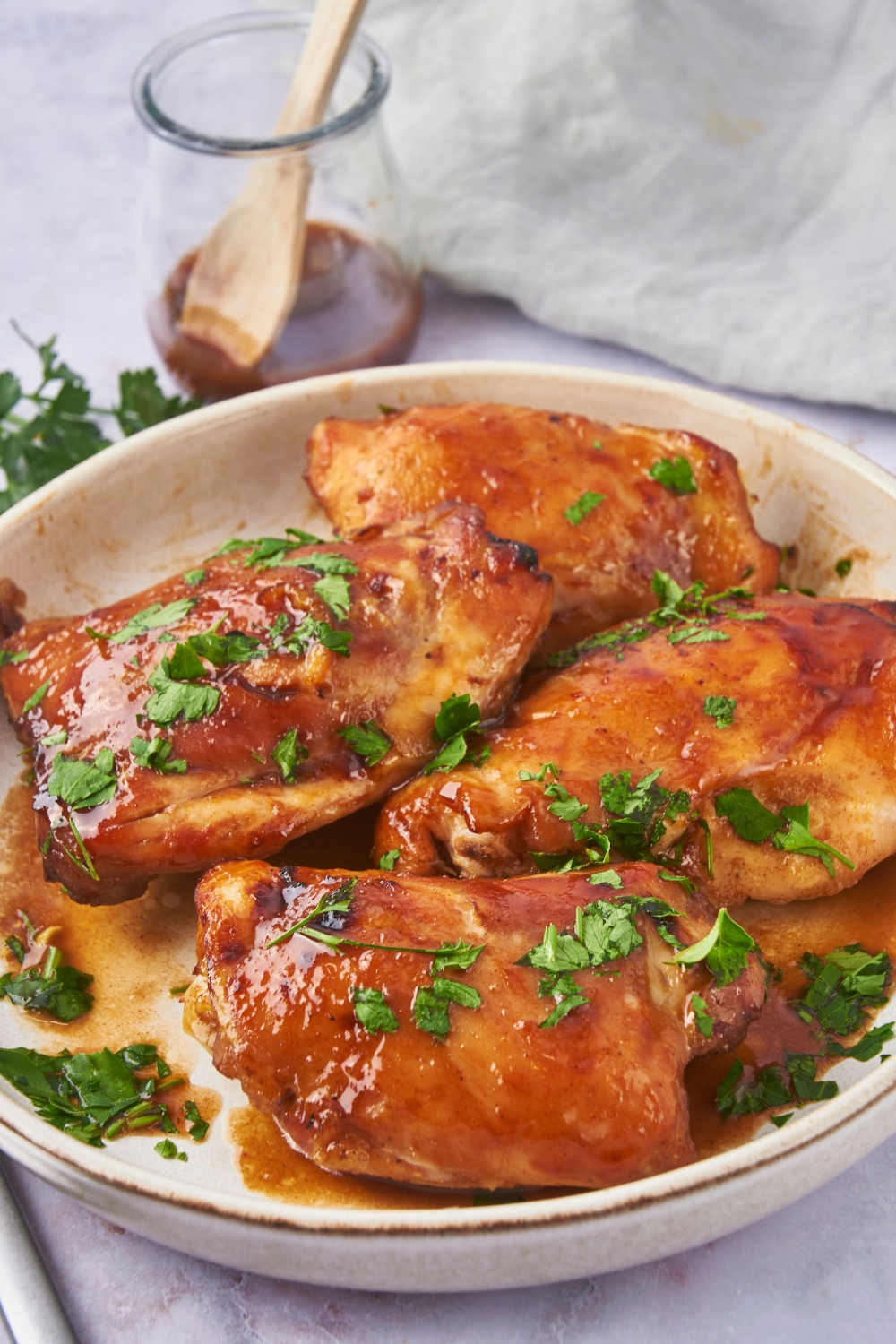 Baked chicken thighs in on a white plate. The chicken is coated in a brown sauce and garnished with fresh herbs.