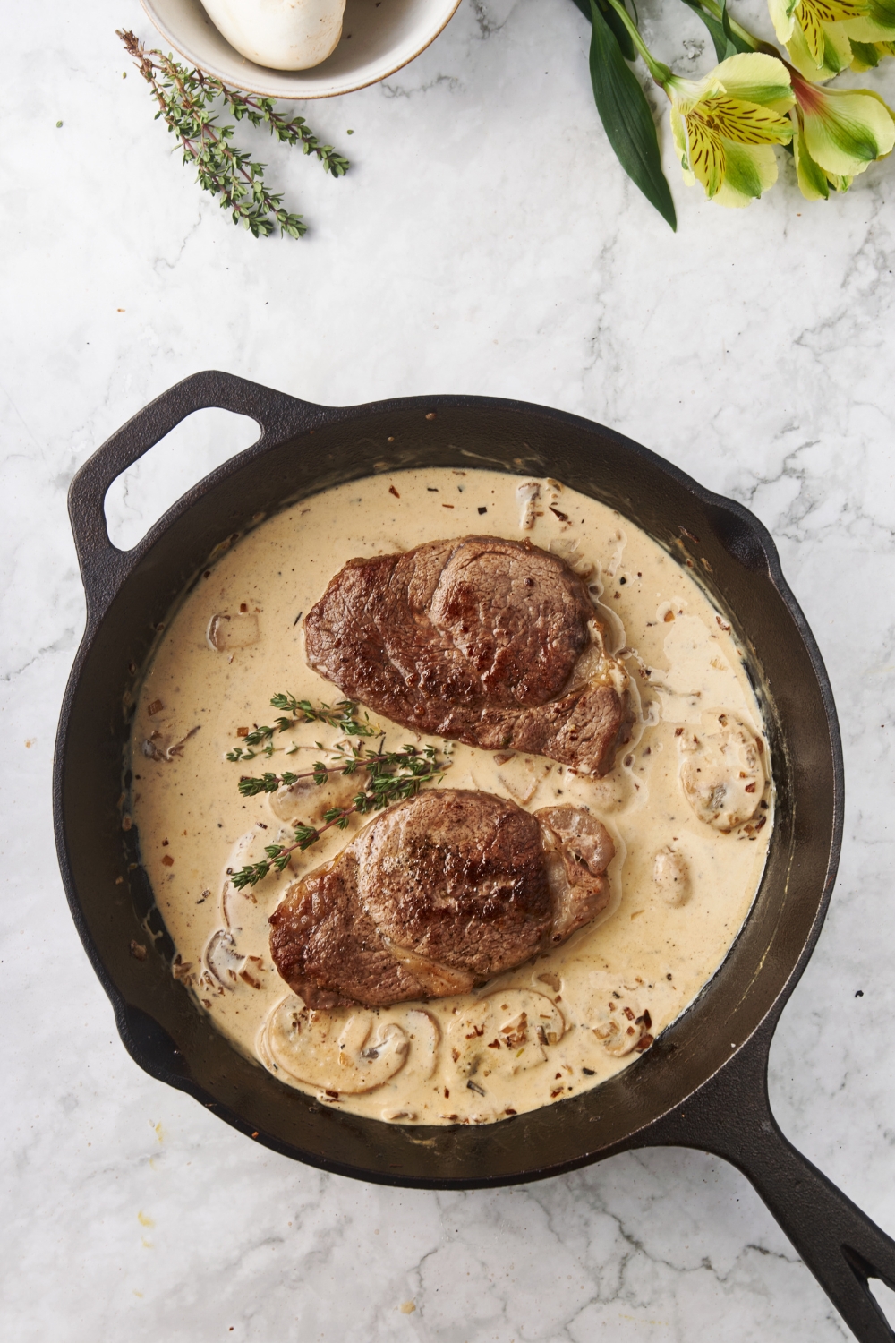 A cast iron skillet with two seared filet mignon steaks and a brown mushroom sauce.