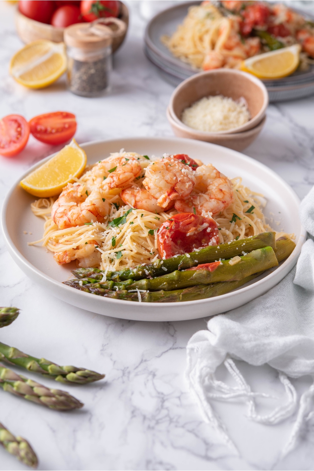 A plate of Olive Garden's shrimp scampi with sides of asparagus, cherry tomatoes, and a lemon wedge. The plate is surrounded by ingredients to make the recipe.