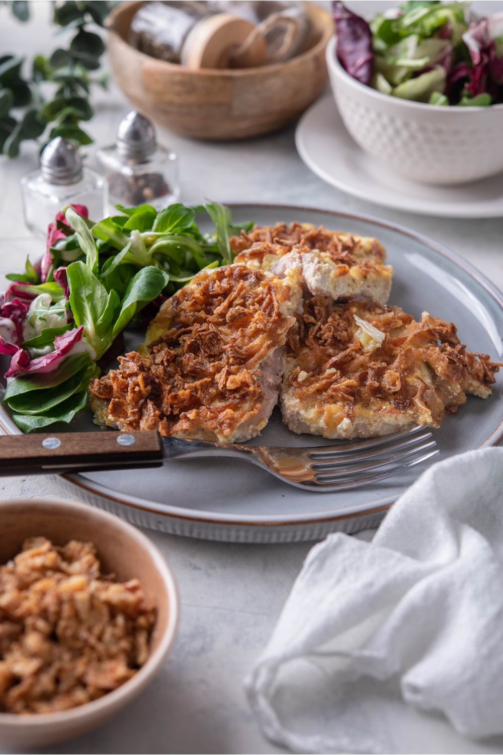 Three french onion pork chops piled on top of each other on a blue plate with a side salad and a fork on the plate.