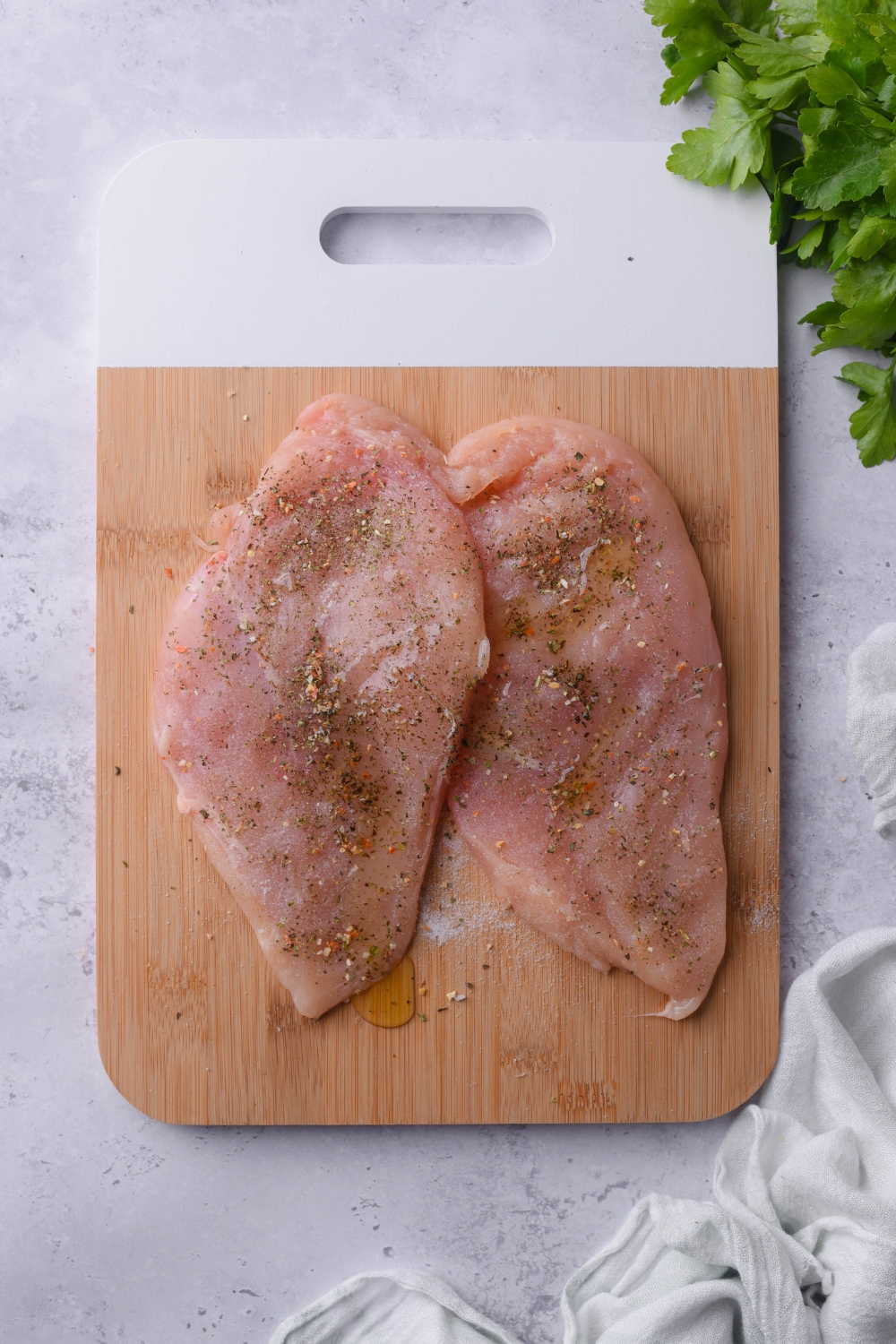 Two raw chicken breast cutlets seasoned with salt and pepper on a wood cutting board.