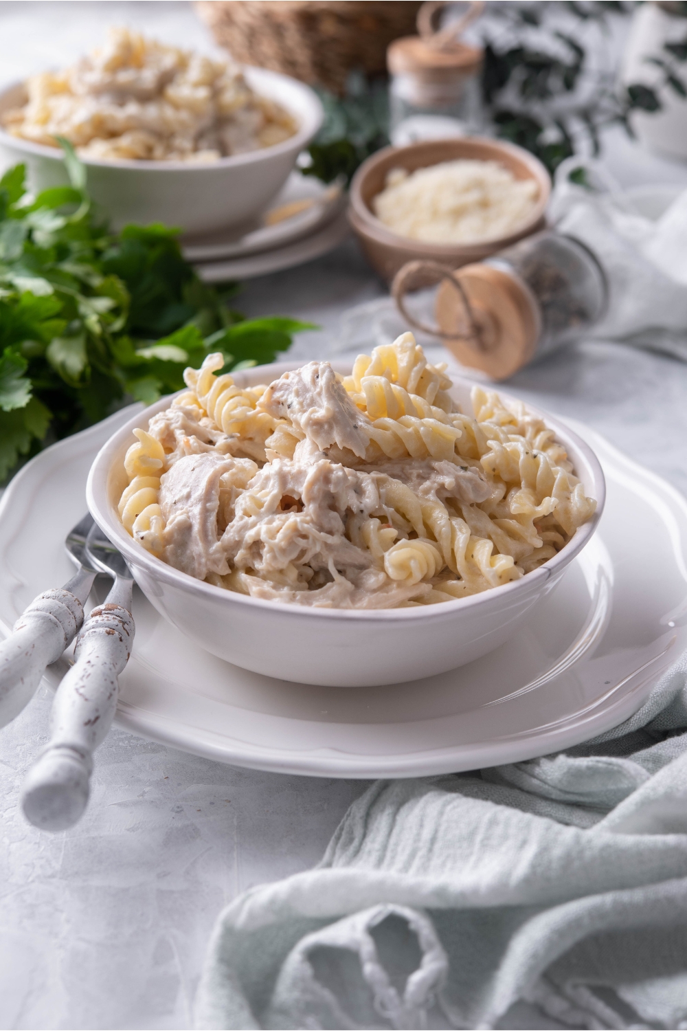 A bowl of pasta and chicken in a cream sauce atop a white plate with two forks next to the bowl of chicken and pasta.