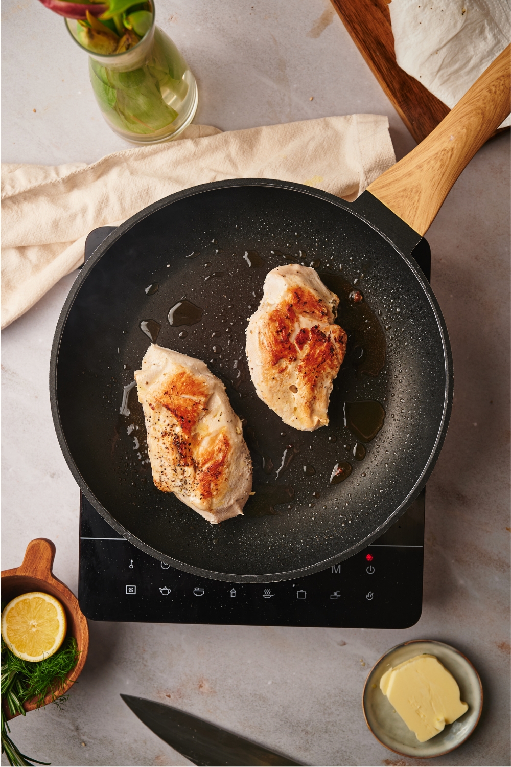 Two seared chicken breasts in a black skillet atop an electric burner.