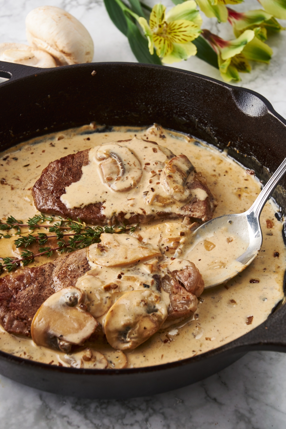 Two seared filet mignon steaks being covered in a brown mushroom sauce with a spoon.