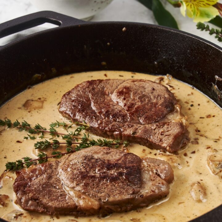 Close up of a cast iron skillet with two seared filet mignon steaks and a brown mushroom sauce.