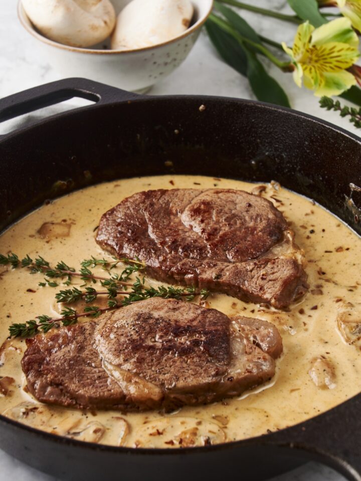 Close up of a cast iron skillet with two seared filet mignon steaks and a brown mushroom sauce.