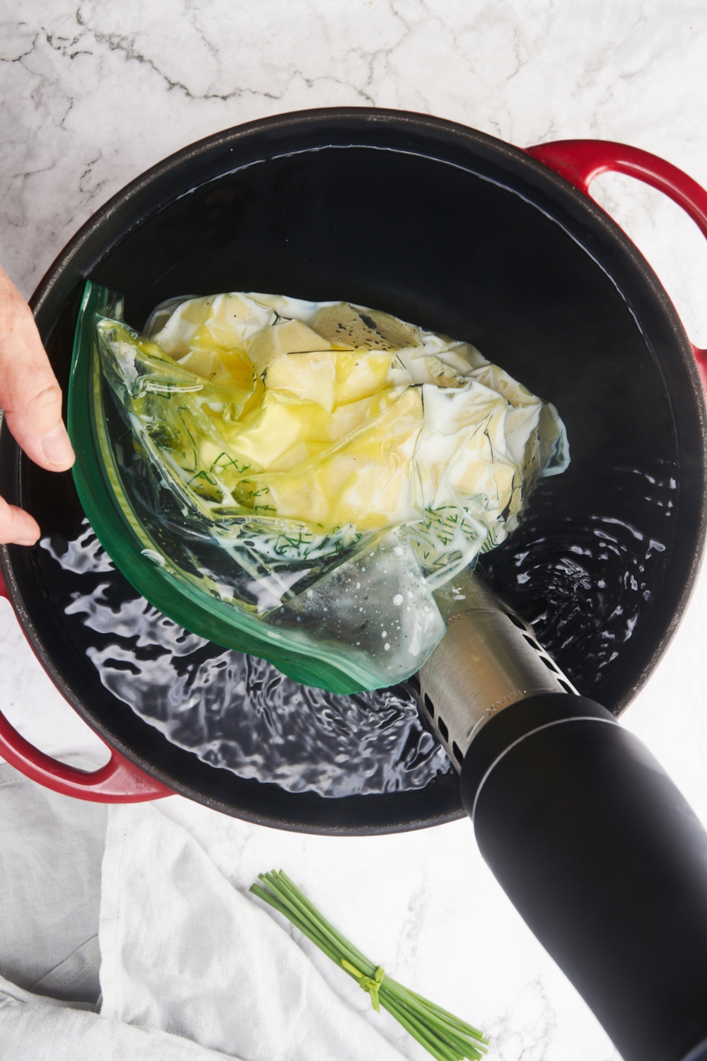 A bag of diced potatoes being placed in a large pot of water with a sous vide machine in it.