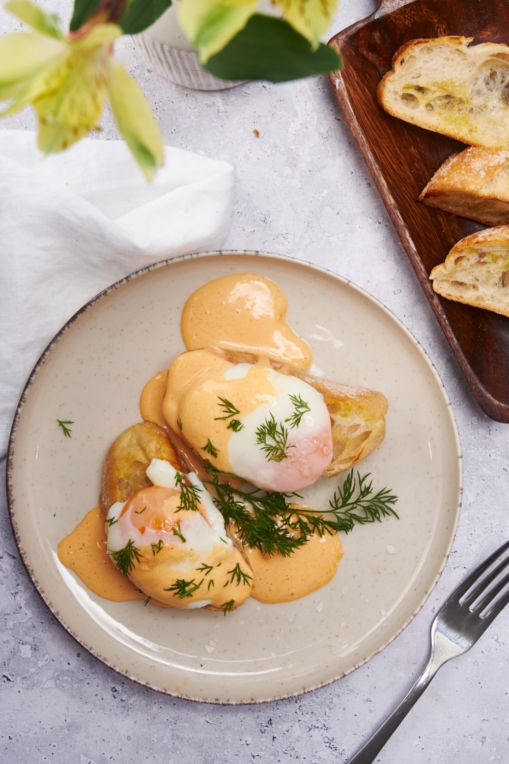 Overhead view of two pieces of toast on a plate, each topped with a poached egg, Hollandaise sauce, and fresh dill.