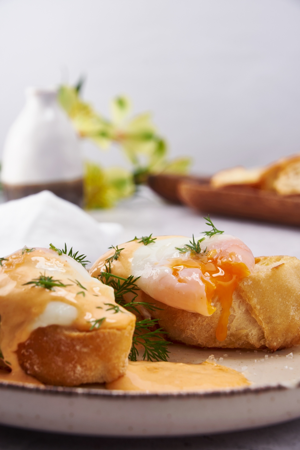 Close up of two pieces of toast on a plate, each topped with a poached egg, Hollandaise sauce, and fresh dill.