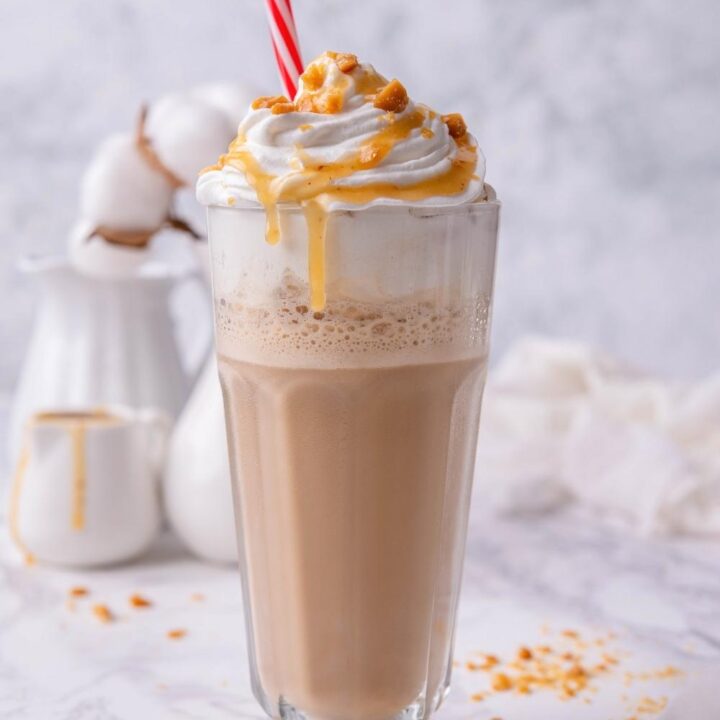 A caramel ribbon crunch frappuccino in a glass with whipped cream and a straw in it.