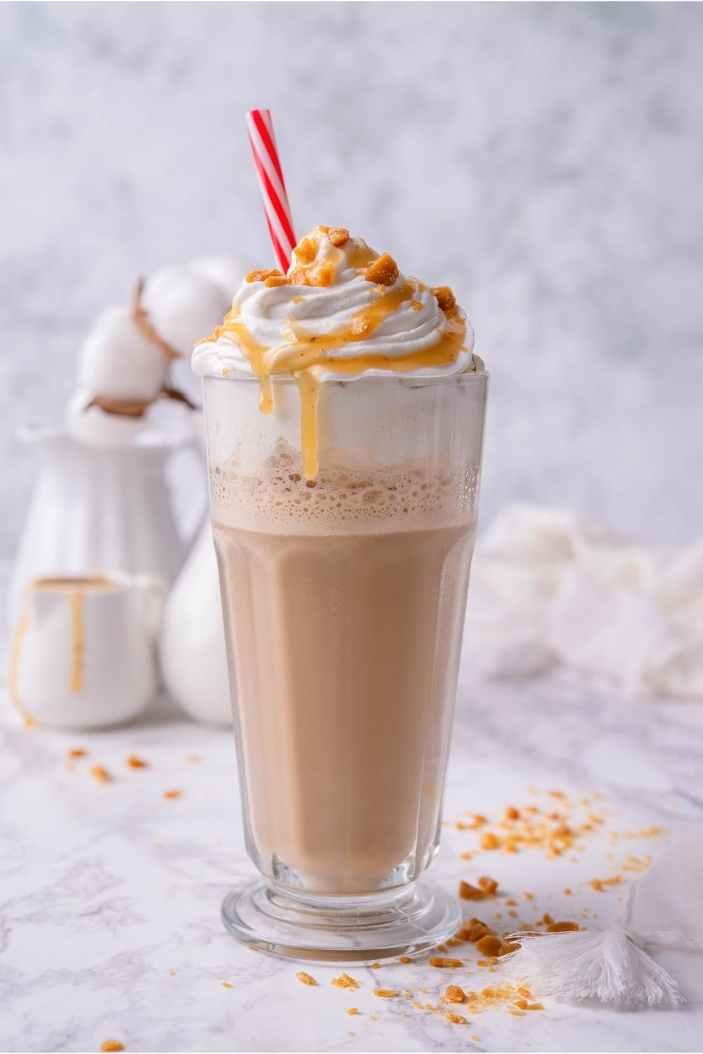 A caramel ribbon crunch frappuccino in a glass with whipped cream and a straw in it.