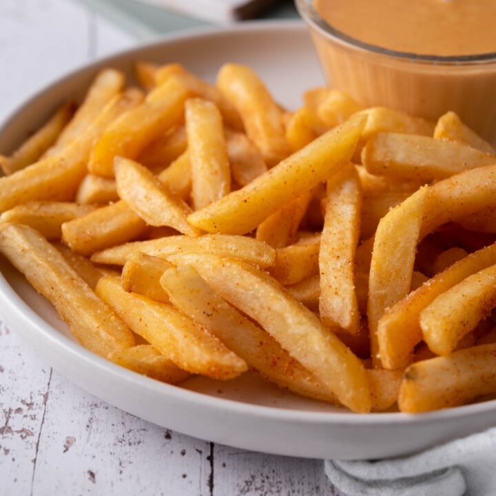 A plate of seasoned french fries with a side of cheese sauce.