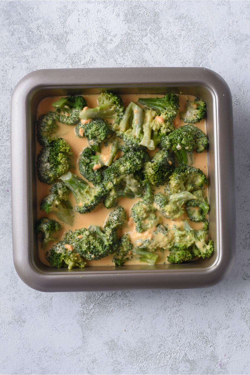 A baking dish filled with unbaked Velveeta cheese and broccoli casserole.