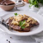 A bunch of caramelized onions on top of liver on a plate.
