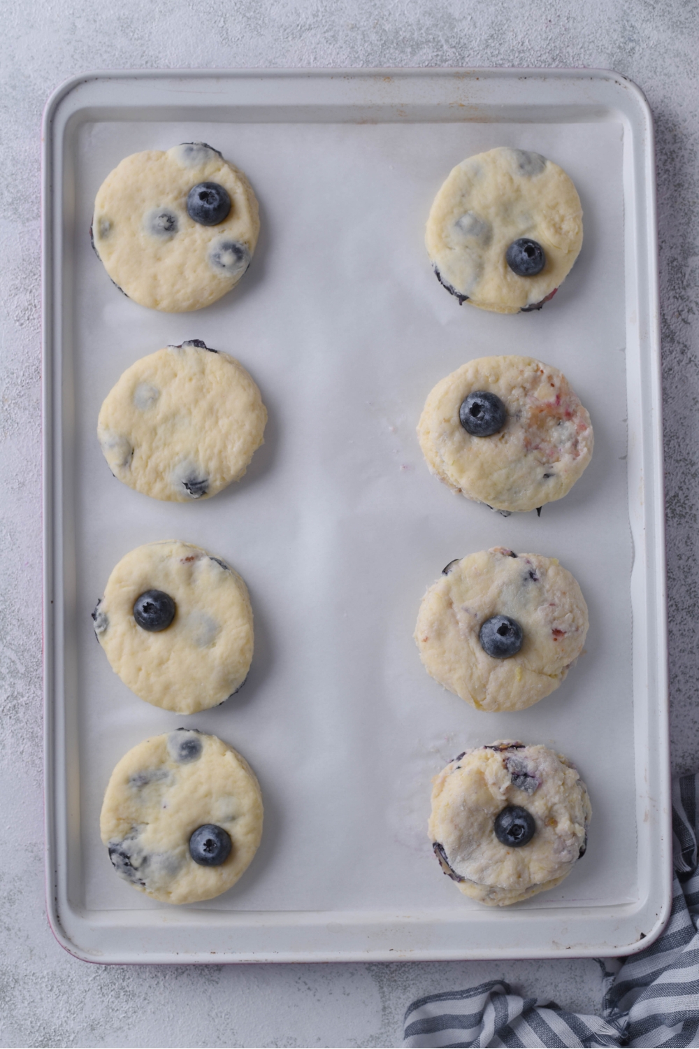 An overhead view of fresh cut out biscuits on a baking sheet lined with parchment paper.
