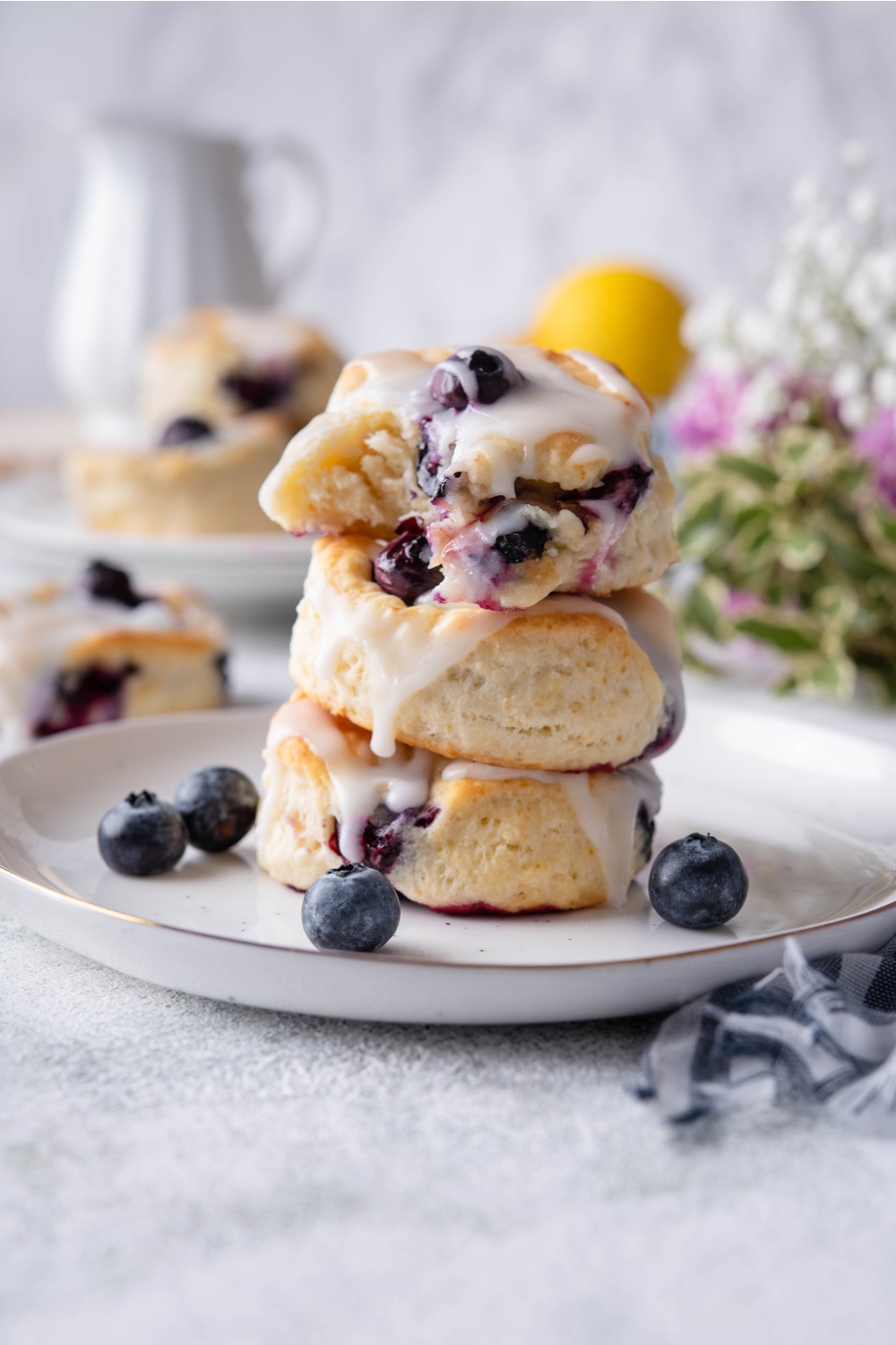 A stack of three blueberry biscuits topped with icing on a plate. The top biscuit has a bite taken out of it.