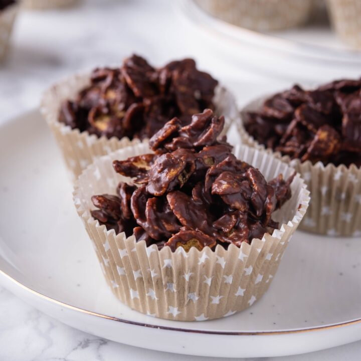 A close up of three chocolate cornflake clusters in muffin liners on a plate.