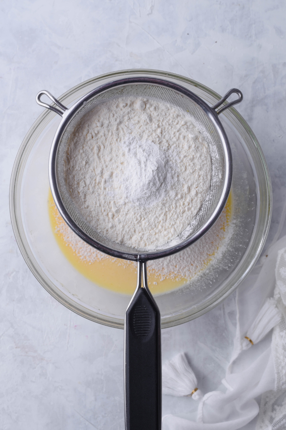 A mixing bowl with a sieve with flour being added to the wet ingredients.