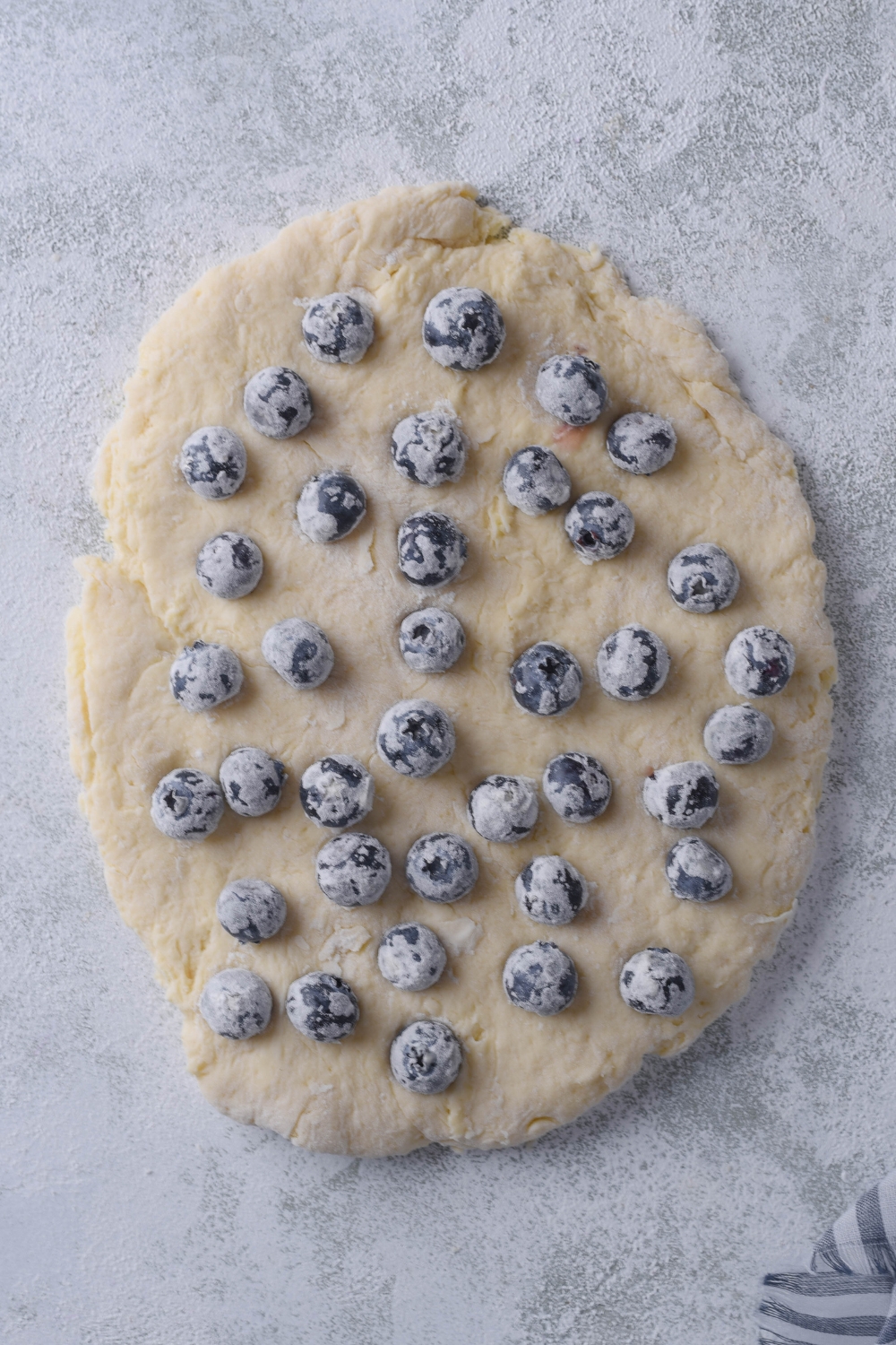 An overhead view of biscuit dough, fresh blueberries have just been added in one layer on it.