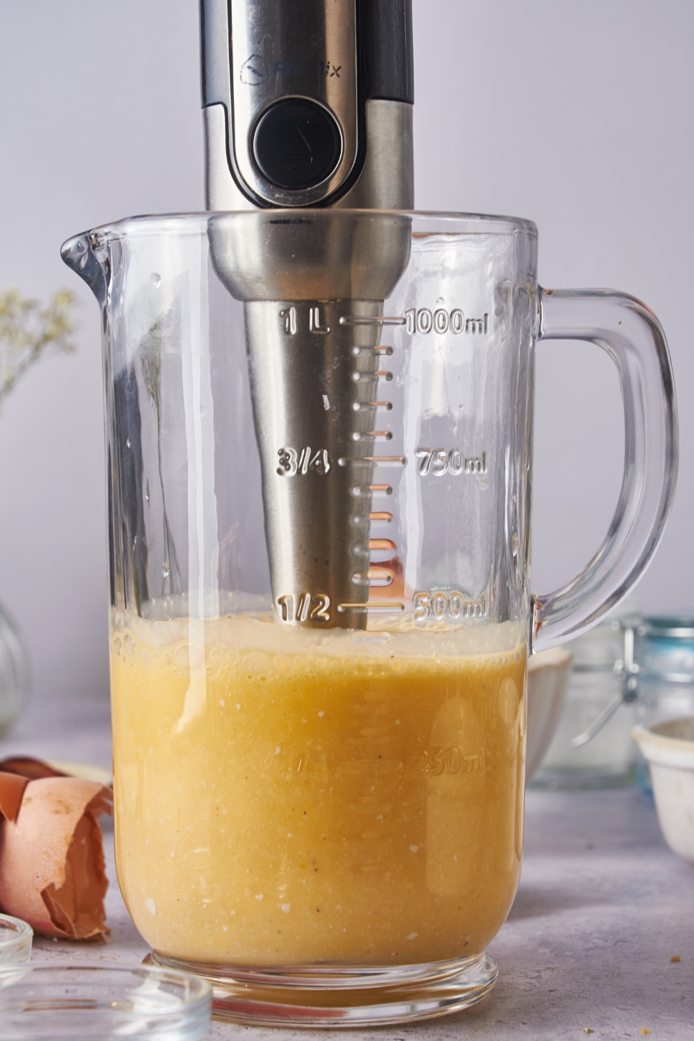 A pitcher with a mix of eggs and cheese being blended by an emersion blender.
