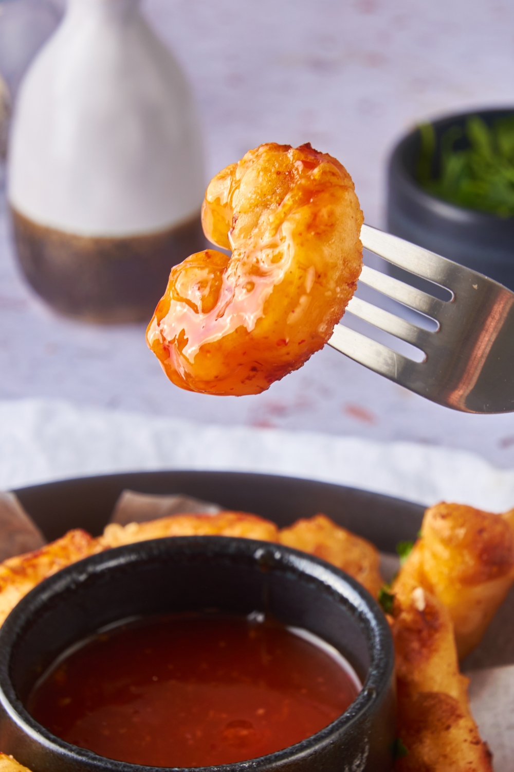 A fork holding a piece of fried shrimp coated in sweet and sour sauce.