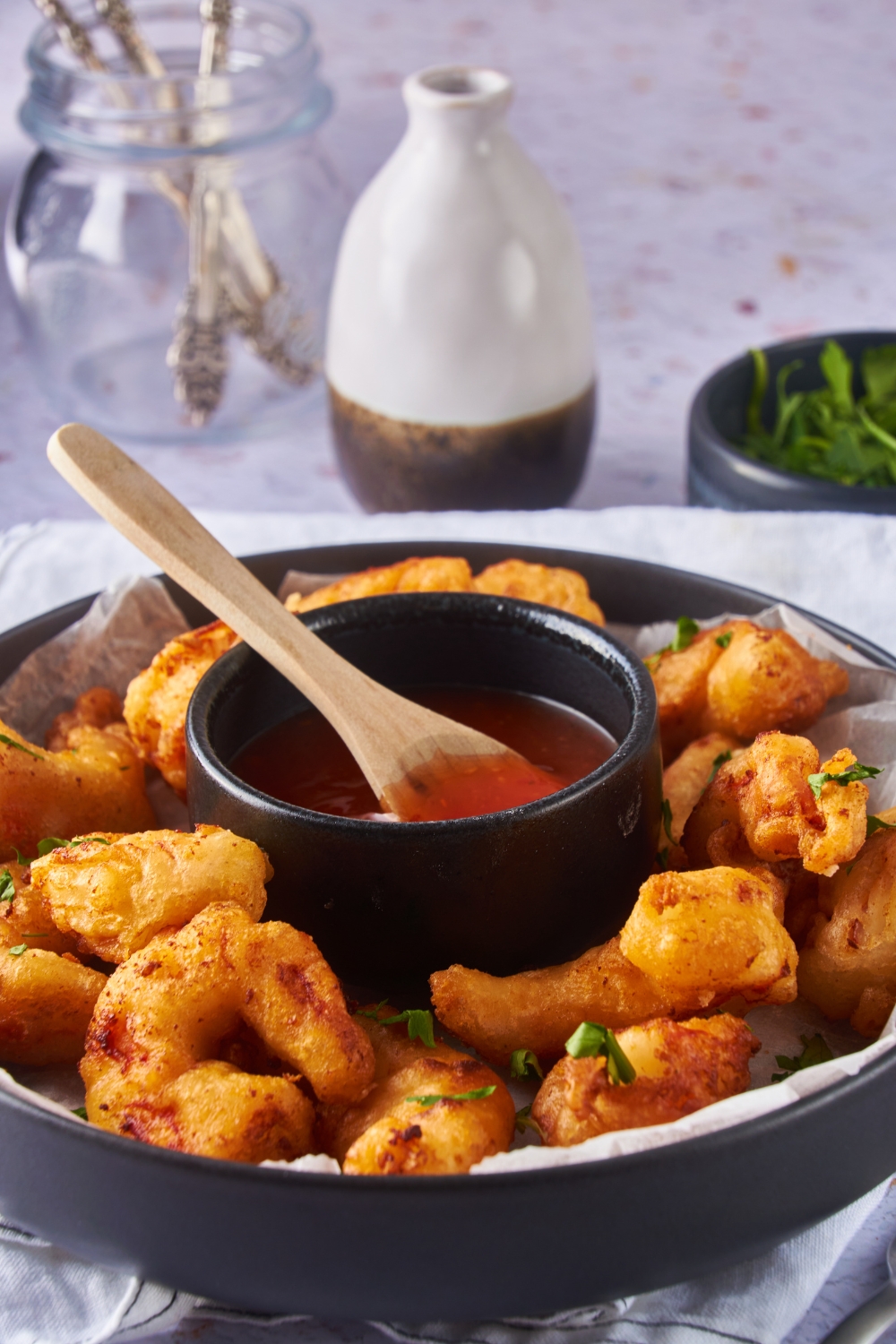 Battered and fried shrimp on a black serving plate garnished with fresh herbs and a bowl of sweet and sour sauce on the plate.