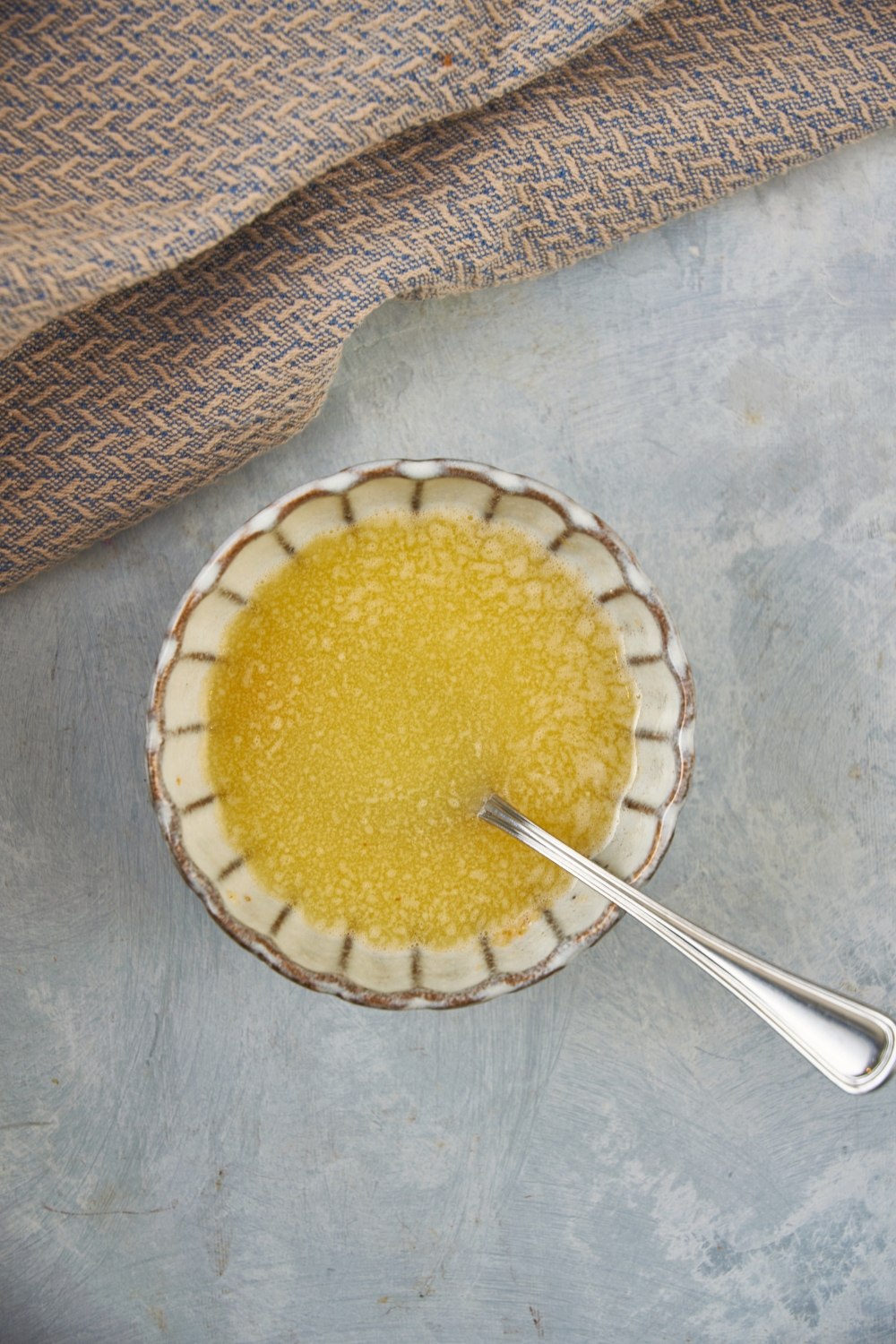 A decorative bowl with melted butter, garlic powder, and a spoon in it.