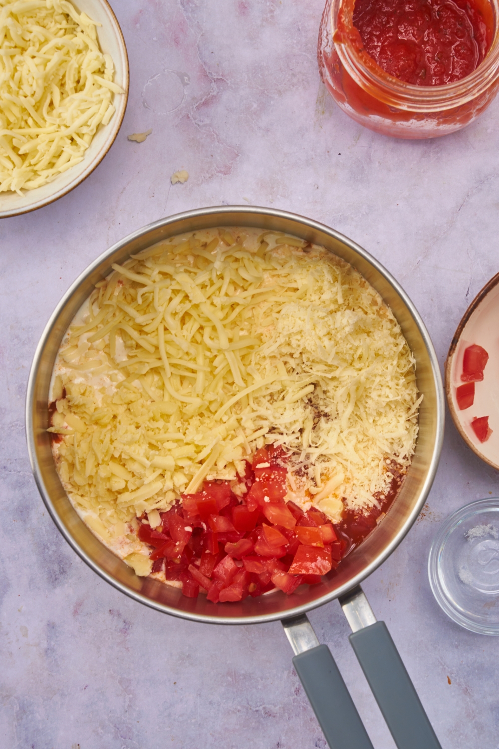 A pot filled with diced tomatoes, marinara sauce, shredded cheese, and cream. The ingredients have not yet been mixed together.