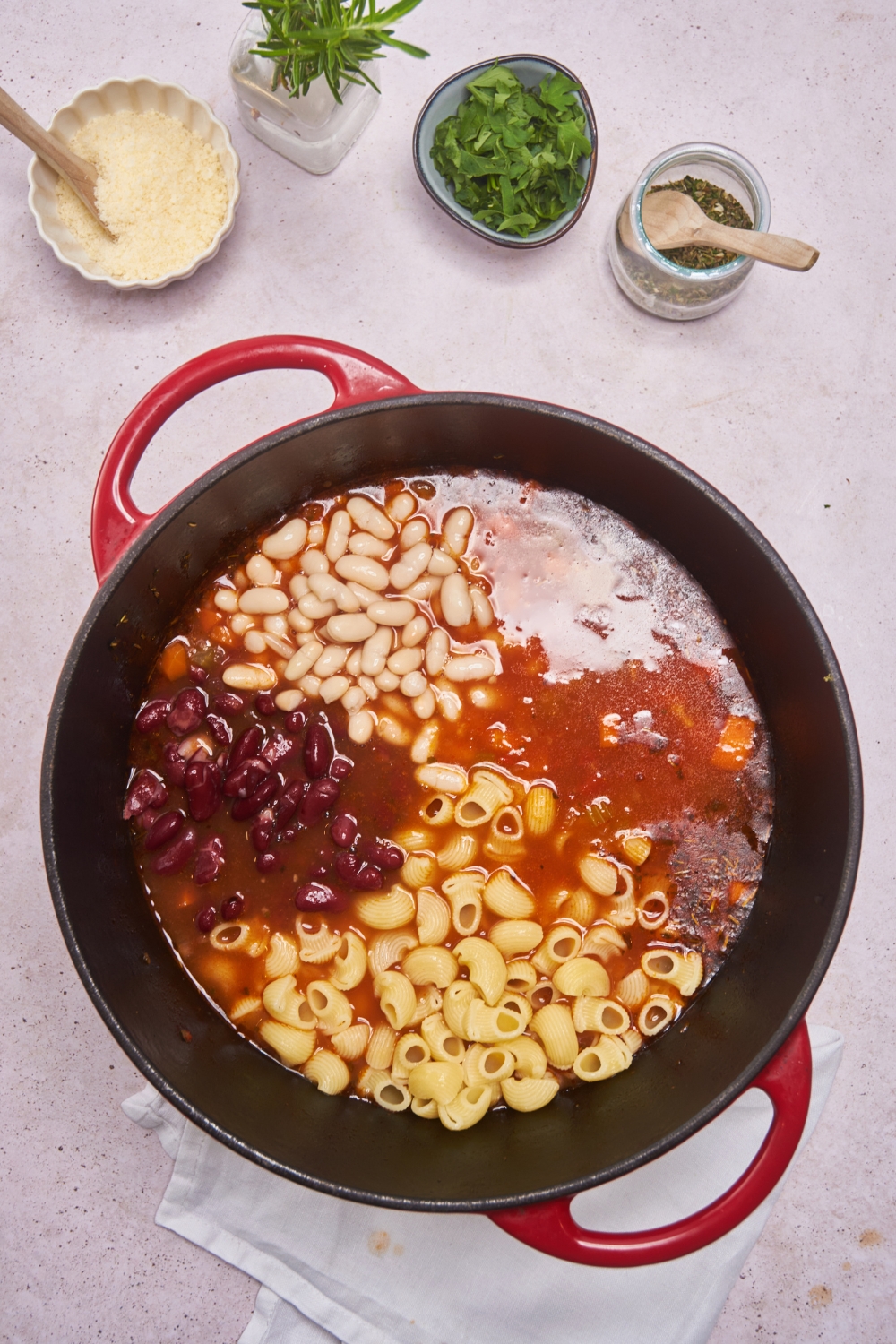 Dutch oven filled with tomato broth, cooked pasta, kidney beans, and northern beans.